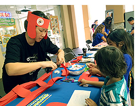PBS Hawaii Board Vice Chair Marissa Sandblom helps assemble Clifford the Big Red Dog headbands for keiki at Kauai’s Parent-Child Fair.